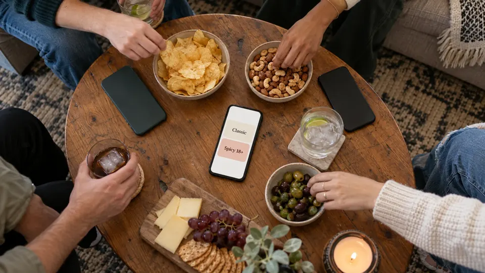 A phone on the table shows the Classic and Spicy 18+ question packs