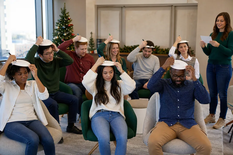 Coworkers drawing Christmas trees on paper plates held on their heads