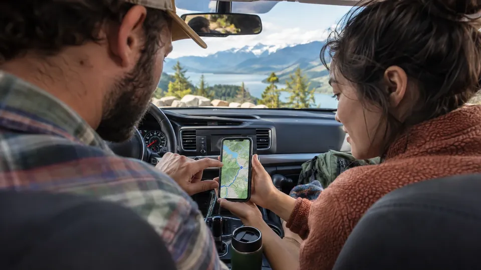 A couple on a road trip in a car looking at a map on a phone, screen sharp