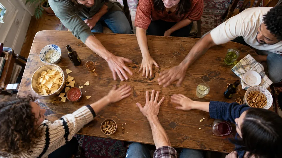 Hands of several friends slapping the table at the same moment, motion, cups and snacks