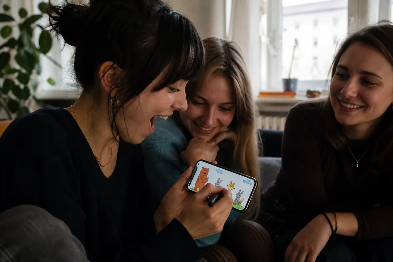 Junge Frau zeigt ihren Freunden lachend eine bunte Tierzeichnung auf dem Handy