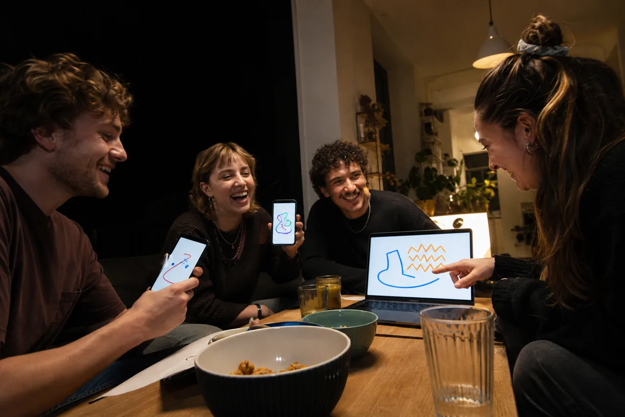 Vier Freunde lachen bei einem Zeichen- und Ratespiel mit Laptop und Handys