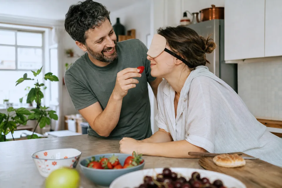 Une femme aux yeux bandés goûte une fraise donnée par son partenaire