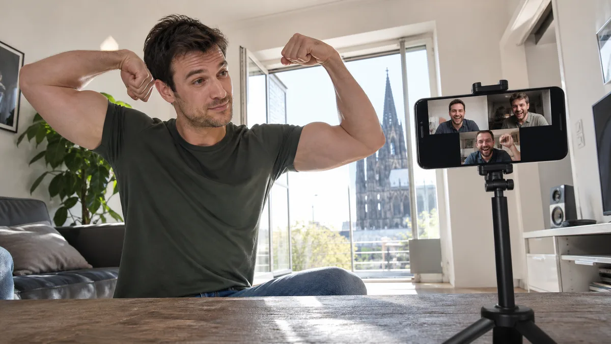 Erwachsener Mann posiert im Video-Call als Bodybuilder vor einem scharfen Handybildschirm