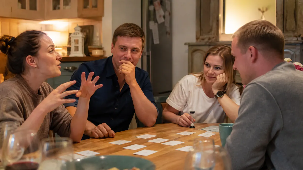 Friends discussing quick guesses around a table with a timer and prompt cards