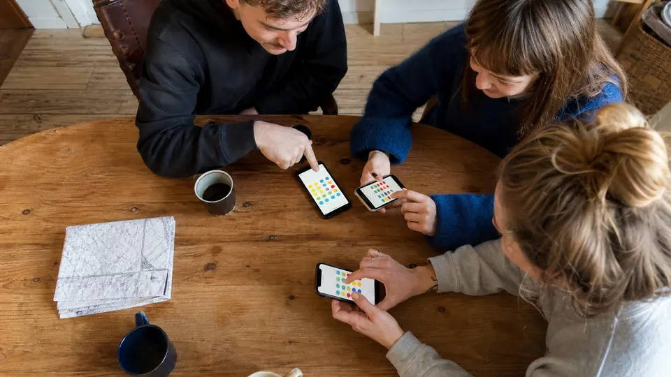 Drei Freunde bearbeiten ein farbiges Spielfeld auf ihren Smartphones